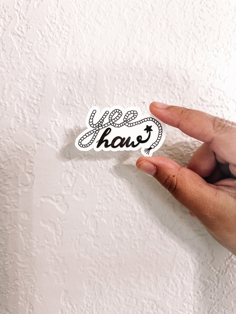May include: A black and white sticker with the text "yee haw" written in a rope-like font. The rope is tied into a knot at the end of the word "haw" and has a star at the end of the knot.