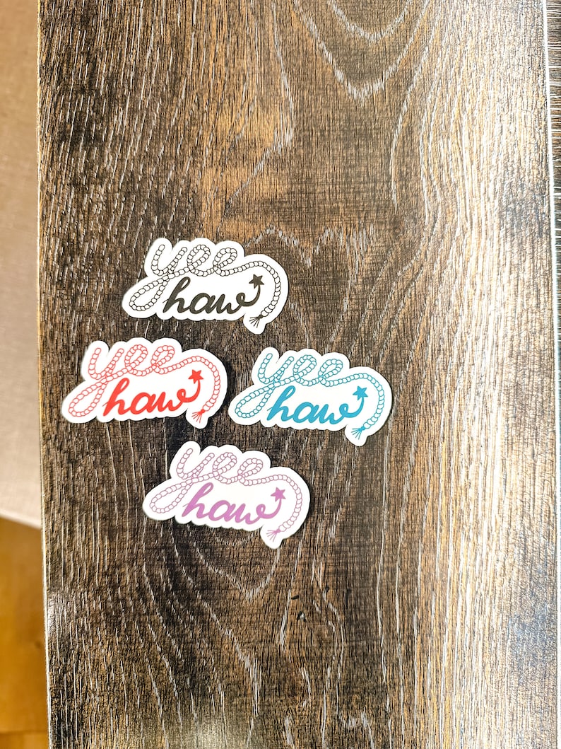 May include: Four stickers with the phrase "yee haw" written in a rope design. The stickers are in different colors: black, pink, blue, and light blue.