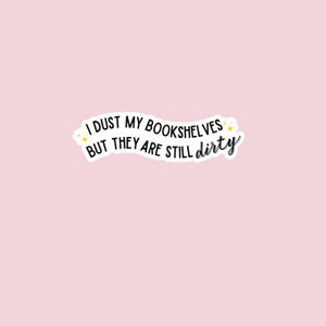 May include: A white sticker with black text that reads "I dust my bookshelves but they are still dirty". The text is curved and has a few small yellow stars on either side.