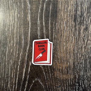 May include: Red book sticker with the text "Thriller Book Club" and a bloody knife sticking out of it.