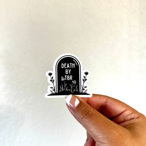 May include: Black and white sticker of a tombstone with the text "DEATH BY TBR" and flowers growing around it.