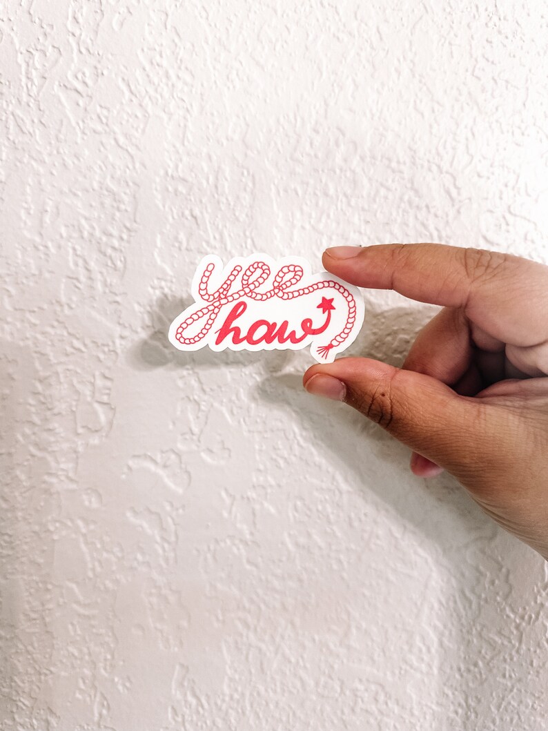 May include: A pink "yee haw" sticker with a rope design. The sticker has a small star at the end of the rope.