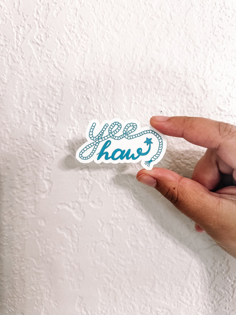 May include: A blue and white sticker with the text "yee haw" written in a rope-like font. A small star is at the end of the word "haw".
