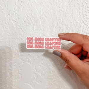 以下が含まれることがあります： 「One More Chapter」というテキストが3回繰り返されたピンクと白のステッカーです。
