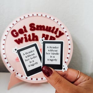 May include: Two white stickers with black text and borders. The stickers are shaped like a rectangle with rounded corners. The text on the stickers reads "A Reader without her kobo is a tragedy" and "A Reader without her kindle is a tragedy".