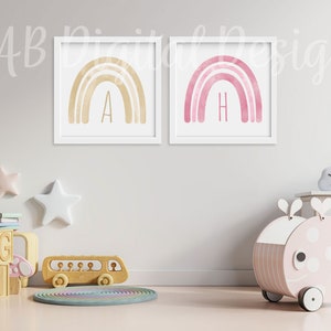 K&ouml;nnte beinhalten: Zwei gerahmte Aquarell-Regenbogen-Drucke mit den Buchstaben A und H in goldener Schrift. Die Drucke h&auml;ngen an einer wei&szlig;en Wand in einem Kinderzimmer mit einem h&ouml;lzernen Spielzeugbus, einem h&ouml;lzernen Spielzeugwal und einem h&ouml;lzernen Bausteinset.