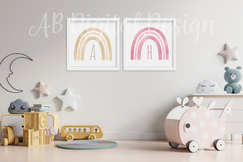 K&ouml;nnte beinhalten: Zwei gerahmte Aquarell-Regenbogen-Drucke mit den Buchstaben A und H in goldener Schrift. Die Drucke h&auml;ngen an einer wei&szlig;en Wand in einem Kinderzimmer mit einem h&ouml;lzernen Spielzeugbus, einem h&ouml;lzernen Spielzeugwal und einem h&ouml;lzernen Bausteinset.