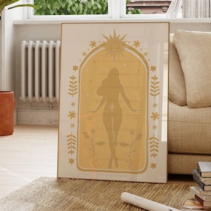 May include: A rectangular framed wall art print featuring a mustard yellow archway design. Inside the arch is a silhouette of a standing figure surrounded by a sun, stars, and floral motifs. The background of the print is a cream color.