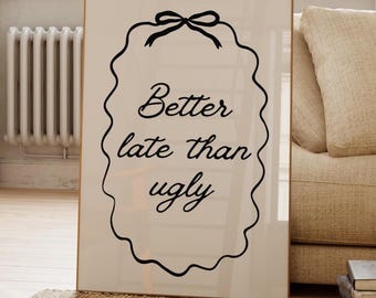 Könnte beinhalten: Ein gerahmter Druck mit dem Text "Better late than ugly" in schwarzer, dekorativer Schrift. Der Druck befindet sich in einem hellen Rahmen und ist an eine Wand gelehnt. Der Hintergrund umfasst ein Fenster, eine Pflanze und ein Sofa.