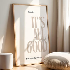 Könnte beinhalten: Gerahmtes Poster mit dem Text "IT'S ALL GOOD" in einer neutralen Farbpalette, das an einer Wand lehnt. Ein kleiner zylindrischer Hocker und ein rundes Bodenkissen befinden sich im Vordergrund. Das Poster hat einen Holzrahmen.