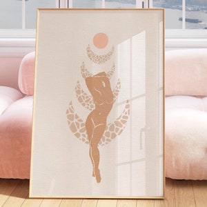May include: A beige framed print featuring a minimalist illustration of a nude figure standing on a crescent moon with a sun above. The print is hanging on a wall above a pink sofa.