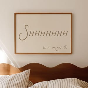 May include: A bedroom interior with a wooden bed frame and striped bedding. A framed print on the wall displays the words "Shhhhhhh Sweet Dreams..." in a script font. The colour scheme is neutral with warm tones.
