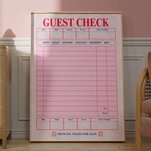 Puede incluir: Un letrero "GUEST CHECK" rosa y blanco enmarcado. El letrero tiene un dise&ntilde;o de cuadr&iacute;cula con espacios para los detalles del pedido. El texto "THANK YOU. PLEASE COME AGAIN" est&aacute; en la parte inferior. El letrero se muestra en una habitaci&oacute;n con un mueble de madera y una pared rosa.