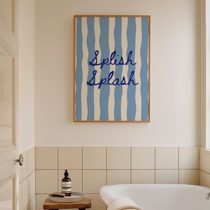 May include: A bathroom interior with a framed print displaying blue and white striped pattern and the words "Splish Splash". A wooden stool supports a tray with a bottle and brush. A white bathtub and a window are also in view.