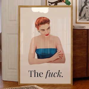 Könnte beinhalten: Ein gerahmter Druck mit einer Frau in einem blauen trägerlosen Oberteil und dem Text "The fuck." Darüber steht auf einem Druck "You up?" und auf einem anderen "New Era Times." Der Raum hat Holzböden und einen dunklen Holzschrank.