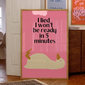 Puede incluir: Un póster rosa enmarcado con el texto "I lied I won't be ready in 5 minutes" y un pato de dibujos animados. Se ven otros dos pósteres enmarcados, uno azul y otro naranja, con texto. La habitación tiene suelos y muebles de madera.