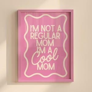 Op de afbeelding: Roze ingelijste print met een witte achtergrond en witte tekst die "Ik ben geen gewone moeder, ik ben een coole moeder" luidt.
