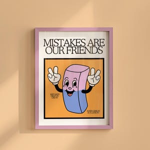 May include: A framed art print with the text "MISTAKES ARE OUR FRIENDS". The artwork features a cartoon eraser character with a smiling face and peace signs. The eraser is pink and blue, set against an orange background.