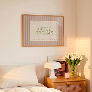 May include: A bedroom scene featuring a bed with white bedding and pillows. A wooden nightstand holds a lamp, a vase of white tulips, and a candle. A framed print with the text "SWEET DREAMS" hangs above the nightstand.