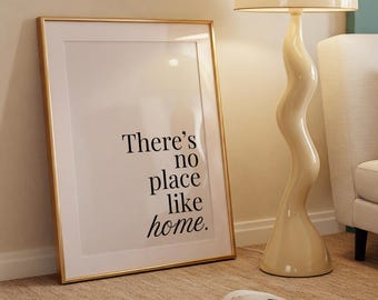 May include: A cream-coloured, mid-century modern floor lamp with a wavy stem and a dome-shaped shade. A framed print with the text "There's no place like home" leans against the wall. A sofa with an orange cushion is in the background.