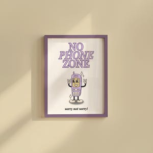 May include: A framed print with a purple border. The print features a cartoon cell phone with a face, arms, and legs, giving a rock-and-roll hand gesture. The words "NO PHONE ZONE" are above the phone, and "sorry not sorry!" is below.