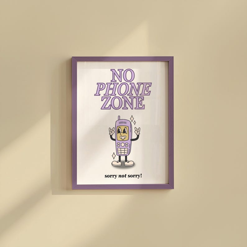 May include: A framed print with a purple border. The print features a cartoon cell phone with a face, arms, and legs, giving a rock-and-roll hand gesture. The words "NO PHONE ZONE" are above the phone, and "sorry not sorry!" is below.