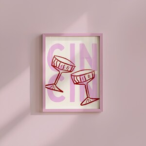 Puede incluir: Una impresi&oacute;n art&iacute;stica enmarcada con un marco rosa, que muestra dos copas de c&oacute;ctel rojas sobre un fondo rosa y crema con la palabra "GIN". La obra de arte tiene un estilo minimalista e ilustrativo, adecuado para una cocina o bar.