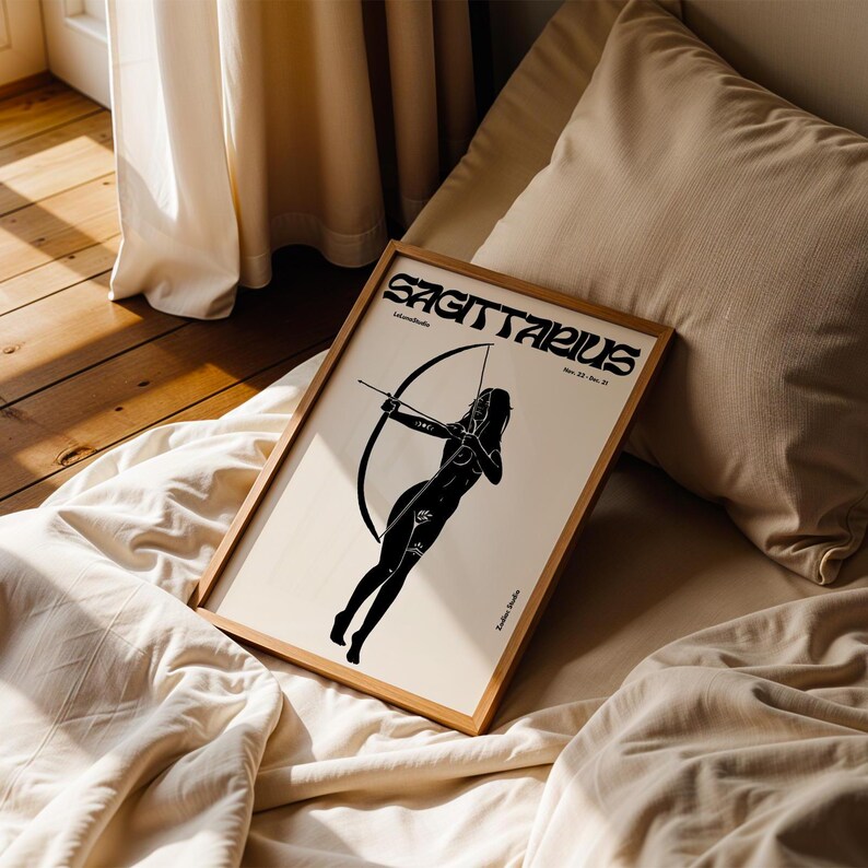 May include: A framed black and white illustration of a Sagittarius zodiac sign. The illustration depicts a woman with an arrow and bow. The frame is made of wood and has a light brown finish. The text "Sagittarius" is printed in black at the top of the illustration.