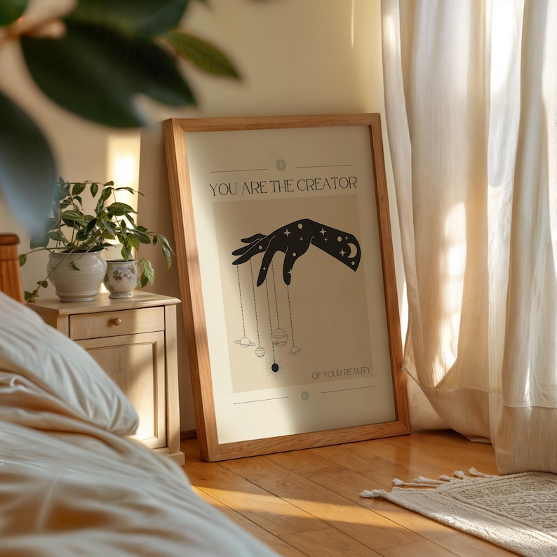 Puede incluir: Un p&oacute;ster beige con una silueta negra de una mano sosteniendo planetas y estrellas. El texto "YOU ARE THE CREATOR OF YOUR REALITY" est&aacute; impreso en el p&oacute;ster.