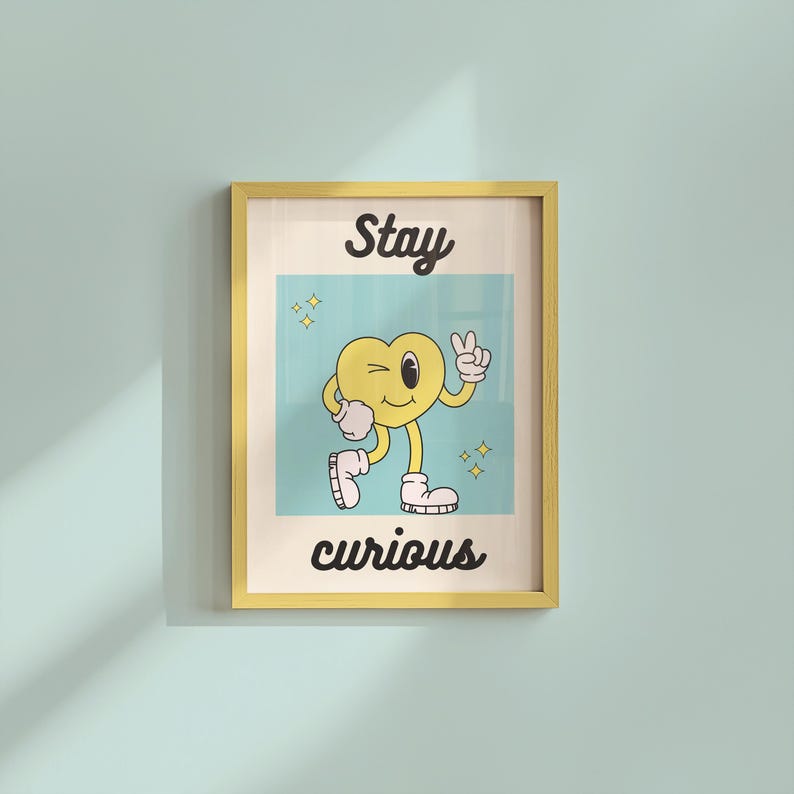 May include: A framed print with a yellow border. The artwork features a cartoon heart character winking and giving a peace sign. The words "Stay curious" are written in black script above and below the heart.