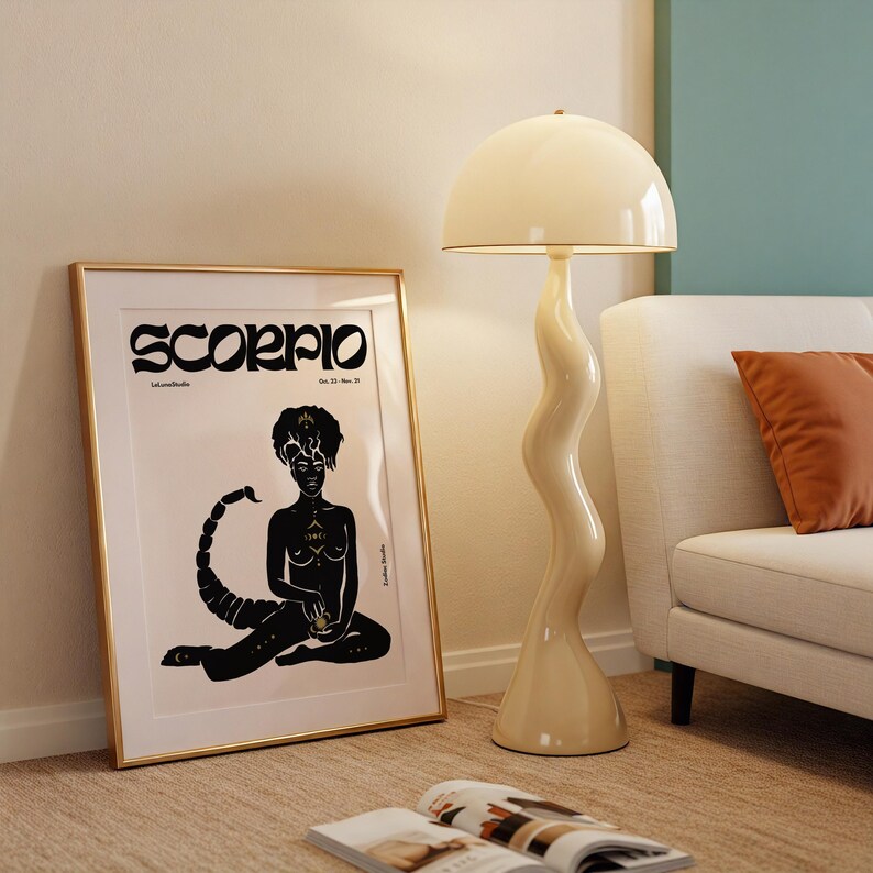 May include: A gold framed poster with a black and gold illustration of a woman sitting with a scorpion tail. The poster has the word "Scorpio" in black text at the top and the dates "Oct. 23 - Nov. 21" in smaller black text below.
