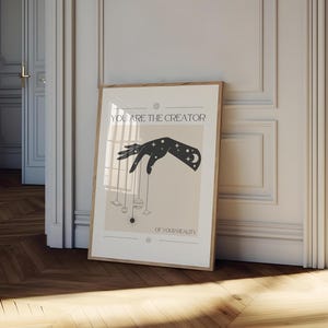 Puede incluir: Un p&oacute;ster beige con una silueta negra de una mano sosteniendo planetas y estrellas. El texto en el p&oacute;ster dice "T&uacute; eres el creador de tu realidad."