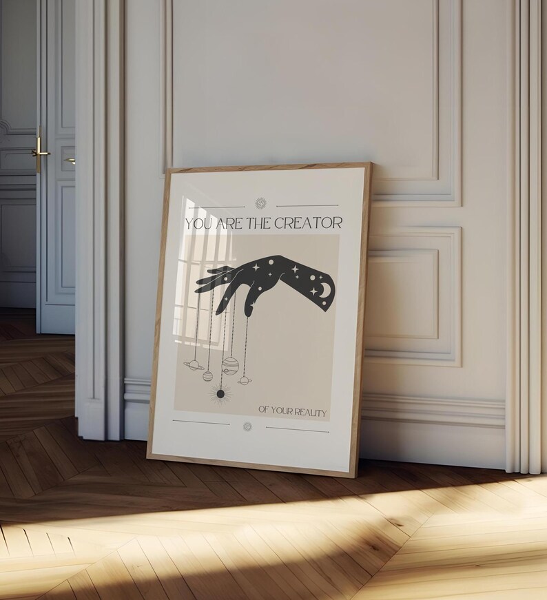 Puede incluir: Un p&oacute;ster beige con una silueta negra de una mano sosteniendo planetas y estrellas. El texto en el p&oacute;ster dice "T&uacute; eres el creador de tu realidad."