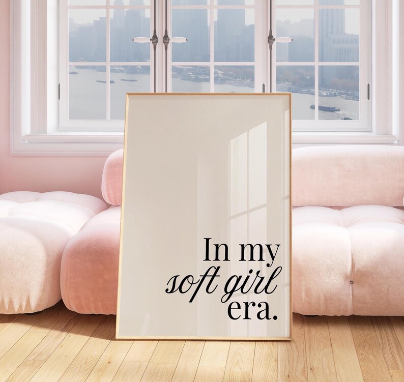 Puede incluir: Una impresi&oacute;n enmarcada con el texto "In my soft girl era." La obra de arte tiene un fondo color crema y un marco dorado. La impresi&oacute;n se exhibe en una habitaci&oacute;n con un sof&aacute; rosa y suelo de madera.