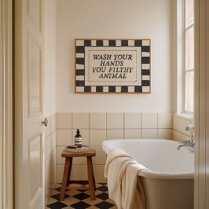 May include: A bathroom scene featuring a framed sign with the text "WASH YOUR HANDS YOU FILTHY ANIMAL." The sign has a black and white checkered border. A wooden stool holds a bottle and brush. A white bathtub and a checkered floor are also visible.