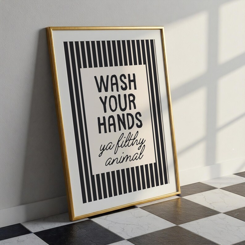 May include: A framed print with a gold border. The artwork features a black and white striped background with a central rectangular panel. The panel displays the text "WASH YOUR HANDS ya filthy animal" in black script.