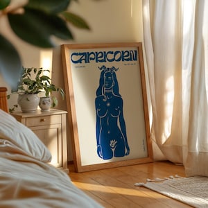 May include: A framed poster with a blue illustration of a woman with horns and a star on her chest. The poster has the text "Capricorn" and "Dec. 22 - Jan. 19" at the top.