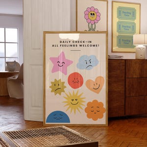 May include: A framed print with the text "DAILY CHECK-IN ALL FEELINGS WELCOME!" and colorful cartoon emotions. Additional framed prints feature a flower and "Reading Time" tickets. The room has wooden floors and furniture.