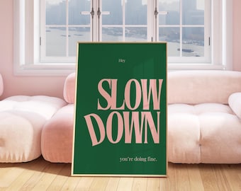 May include: A framed art print with a gold border. The print has a dark green background with the words "SLOW DOWN" in large, pink, sans-serif font. The text "Hey" and "you're doing fine" are also included.