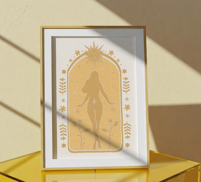 May include: A framed wall art print featuring a mustard yellow archway design. Inside the arch is a silhouette of a person standing with arms outstretched, surrounded by a sun, stars, and floral motifs. The frame is a light wood color.