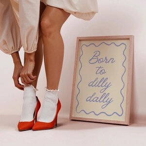 May include: A framed print with the text "Born to dilly dally" in blue script. The image also shows a pair of orange high heels and white socks with a ruffle trim.