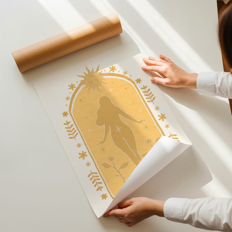 May include: A rectangular white poster featuring a gold-colored illustration of a human silhouette centered within an arched frame. The design includes a sun at the top, surrounding floral and star motifs, and a brown cardboard mailing tube nearby.