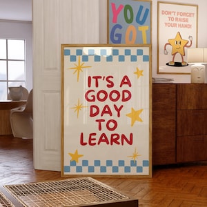 May include: A framed poster with the text "IT'S A GOOD DAY TO LEARN" in red, with yellow star accents and a blue and white checkered border. Two other framed posters are visible, one with "YOU GOT" and another with a cartoon star.