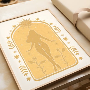 May include: A framed rectangular wall art print featuring a mustard yellow archway design. Inside the arch is a silhouette of a figure surrounded by celestial elements including a sun, stars, and botanical motifs like leaves and flowers.