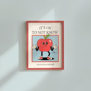 May include: A framed print featuring a cartoon apple character with a sad expression, arms outstretched. The text "IT'S OK TO NOT KNOW" is above the apple, with "THAT'S WHY WE ARE HERE" below. The frame is a reddish-pink color.