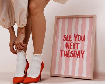May include: Orange high heels with white ruffled socks. A framed print with pink and white stripes and the text "SEE YOU NEXT TUESDAY" in red. The image is set against a neutral background.