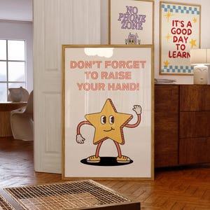 May include: A framed poster with the text "DON'T FORGET TO RAISE YOUR HAND!" and a cartoon star character. Two other framed posters are visible, one with "NO PHONE ZONE" and another with "IT'S A GOOD DAY TO LEARN". The posters are in a room with wooden floors.