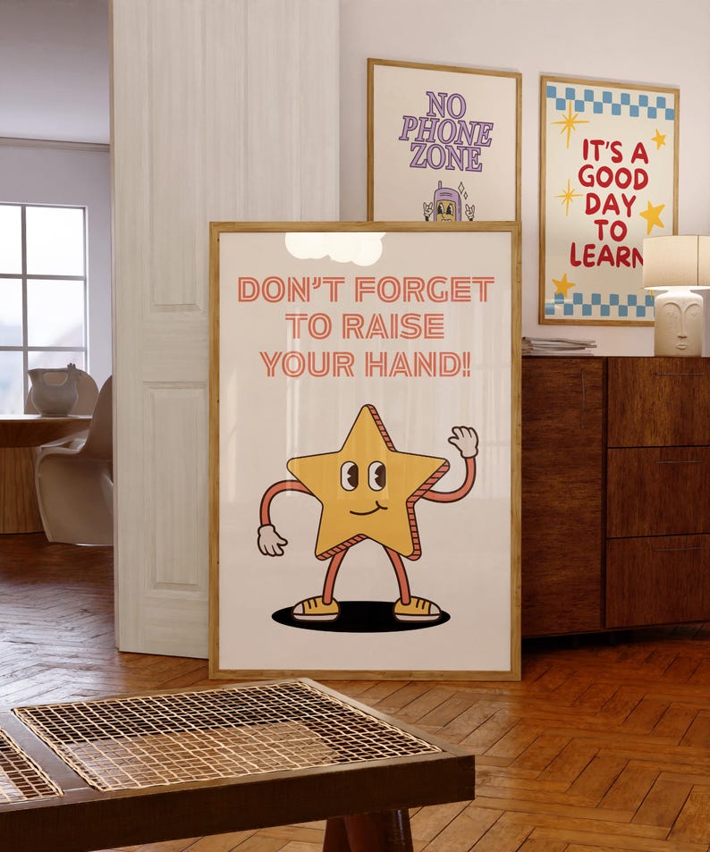 May include: A framed poster with the text "DON'T FORGET TO RAISE YOUR HAND!" and a cartoon star character. Two other framed posters are visible, one with "NO PHONE ZONE" and another with "IT'S A GOOD DAY TO LEARN". The posters are in a room with wooden floors.