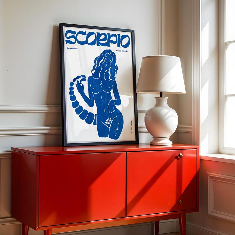 Pode incluir: Uma impress&atilde;o azul e branca de uma mulher com uma cauda de escorpi&atilde;o, com a palavra "Scorpio" em letras negritas no topo. A impress&atilde;o est&aacute; emoldurada em uma moldura preta e est&aacute; pendurada em uma parede branca acima de um arm&aacute;rio vermelho.