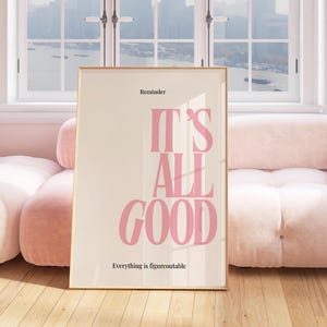 以下が含まれることがあります： クリーム色の背景にピンク色の「It's All Good」という言葉が書かれた額入りのポスター。上部には「Reminder」、下部には「Everything is figureoutable」と書かれています。ポスターはピンク色のソファに立てかけられています。